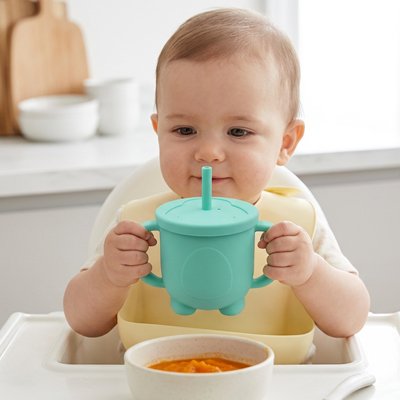 Bébé-à table admire son gobelet bebe vert