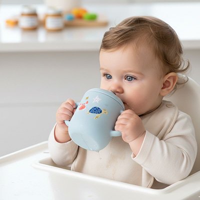 Bébé à table buvant dans  son gobelet bébé bleu