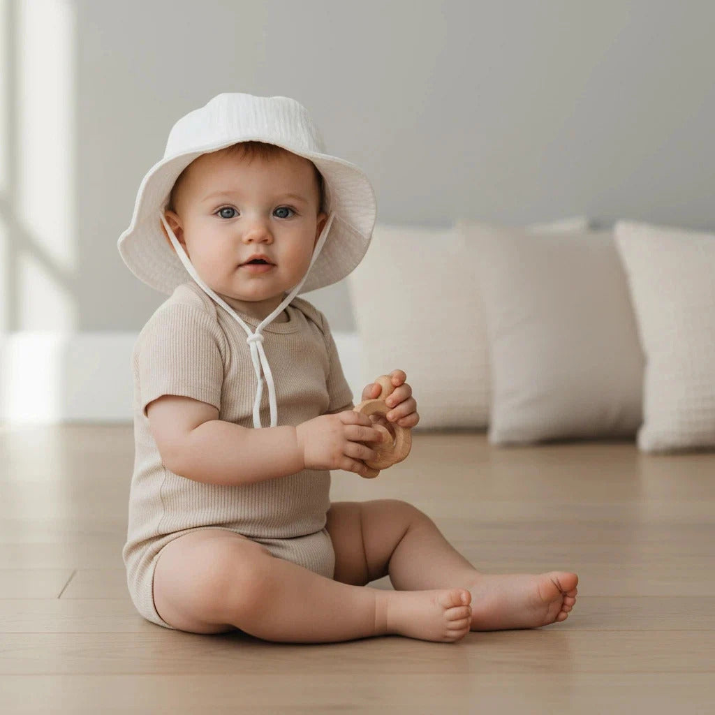 Bébé assis en chambre portant son chapeau bebe blanc