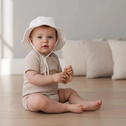 Bébé assis en chambre portant son chapeau bebe blanc