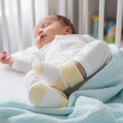 bébé dort avec chaussette bébé jaune blanc dans son berceau