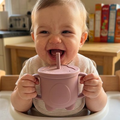 Bébé heureux boit son jus dans gobelet bebe rose