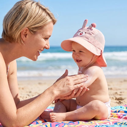 Bébé porte chapeau bebe rose en plage avec maman