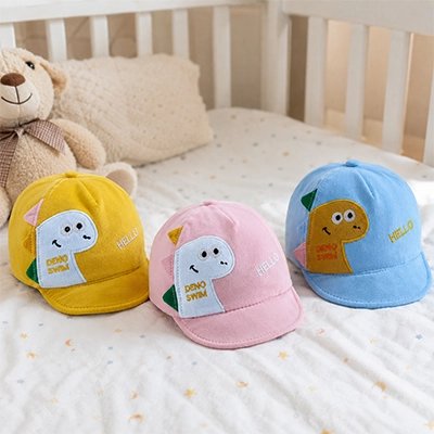 Casquette bebe jaune rose et bleu dinosaure dans le berceau