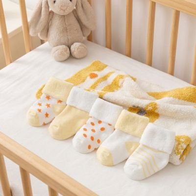 cinq paires chaussette bébé jaune blanc posé  dans un berceau