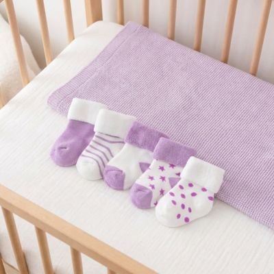 cinq paires chaussette bébé violet blanc posé dans  un berceau