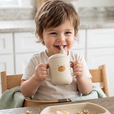 Enfant souriant à table buvant dans son gobelet bebe beige