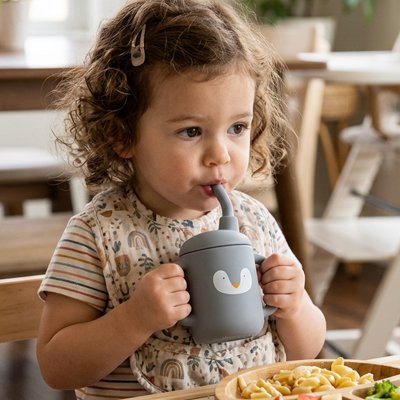 Fillette à table buvant dans son gobelet bebe gris