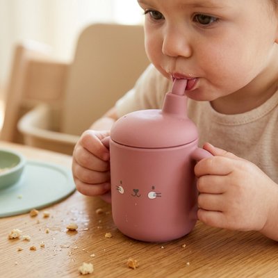 Fillette à table buvant dans son gobelet bebe rose