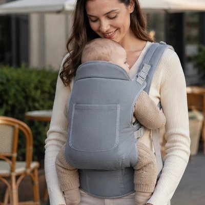 Maman sourit à bébé dans porte bébé gris