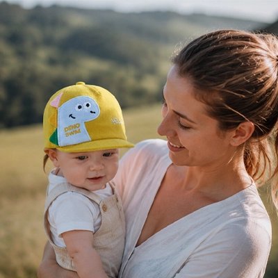 Maman sourit à bébé portant casquette bebe jaune dinosaure