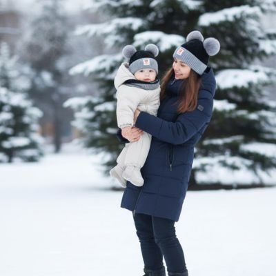 Maman tient bébé portant bonnet bebe noir gris dans neige 
