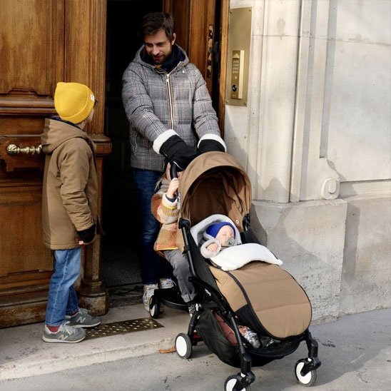 Papa devant porte avec bébé dans chancelière poussette marron blanc